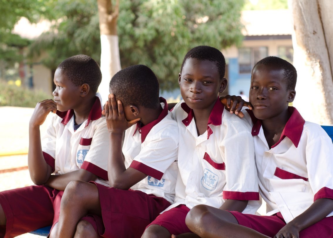 Cinque giovani in uniforme scolastica seduti su una panchina.