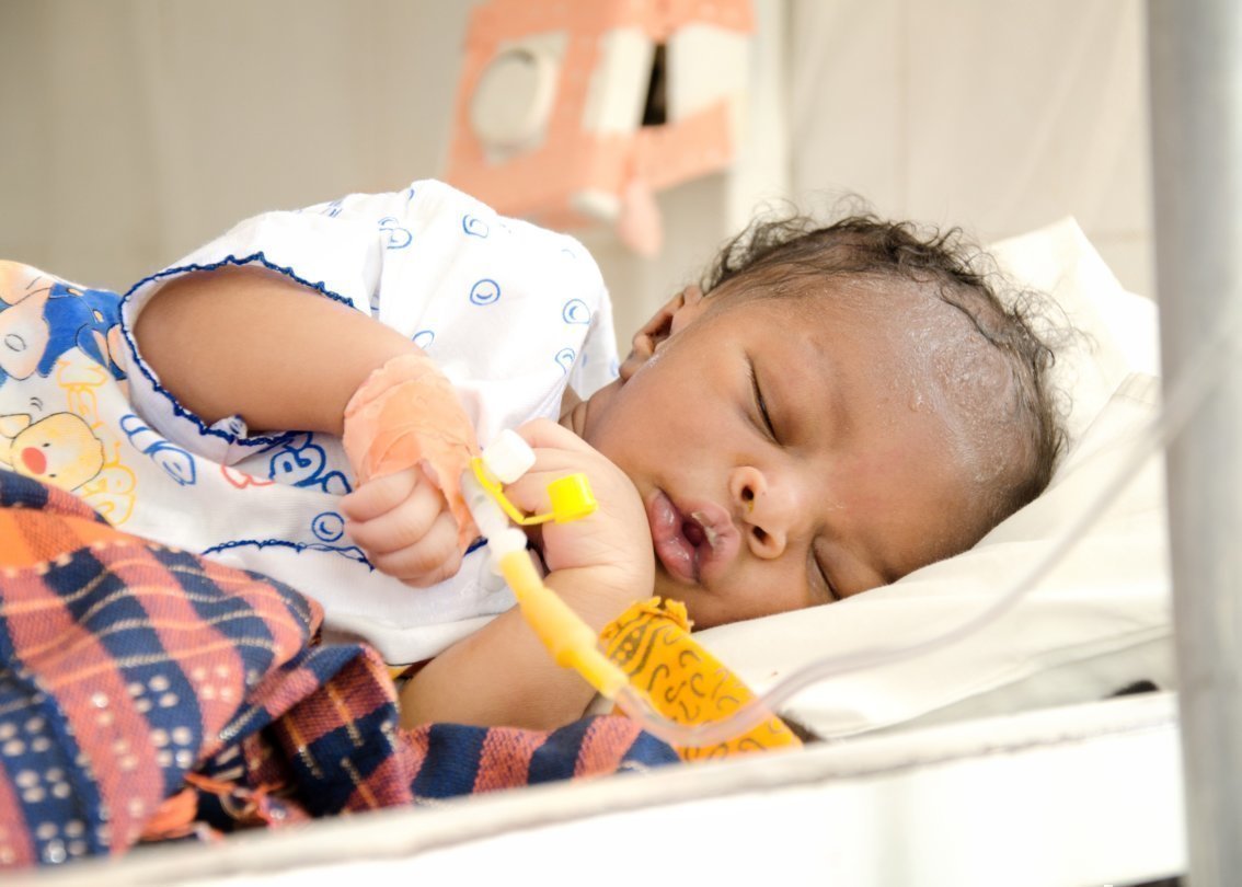 Un neonato dorme con un attacco per flebo nella mano.